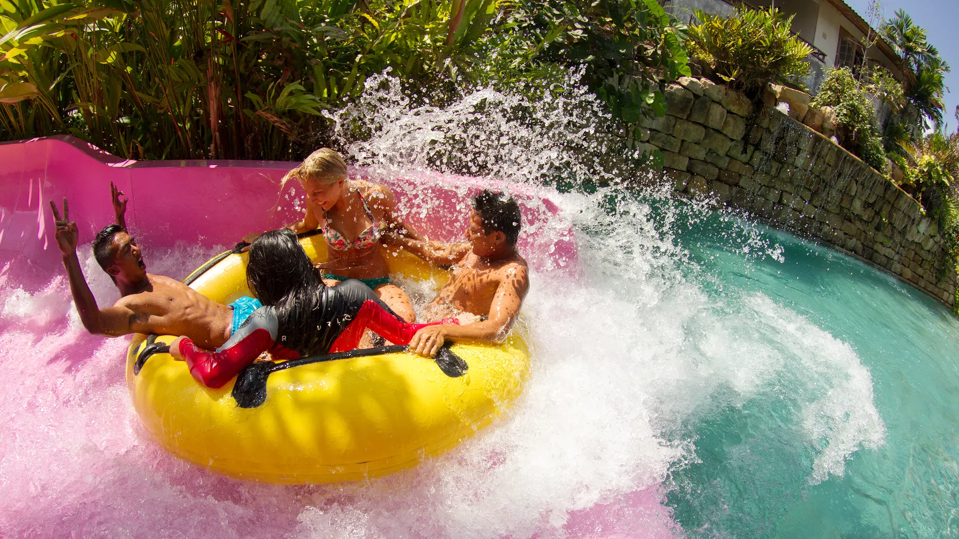 Four friends splashing down a raft slide on a yellow tube at Waterbom Bali