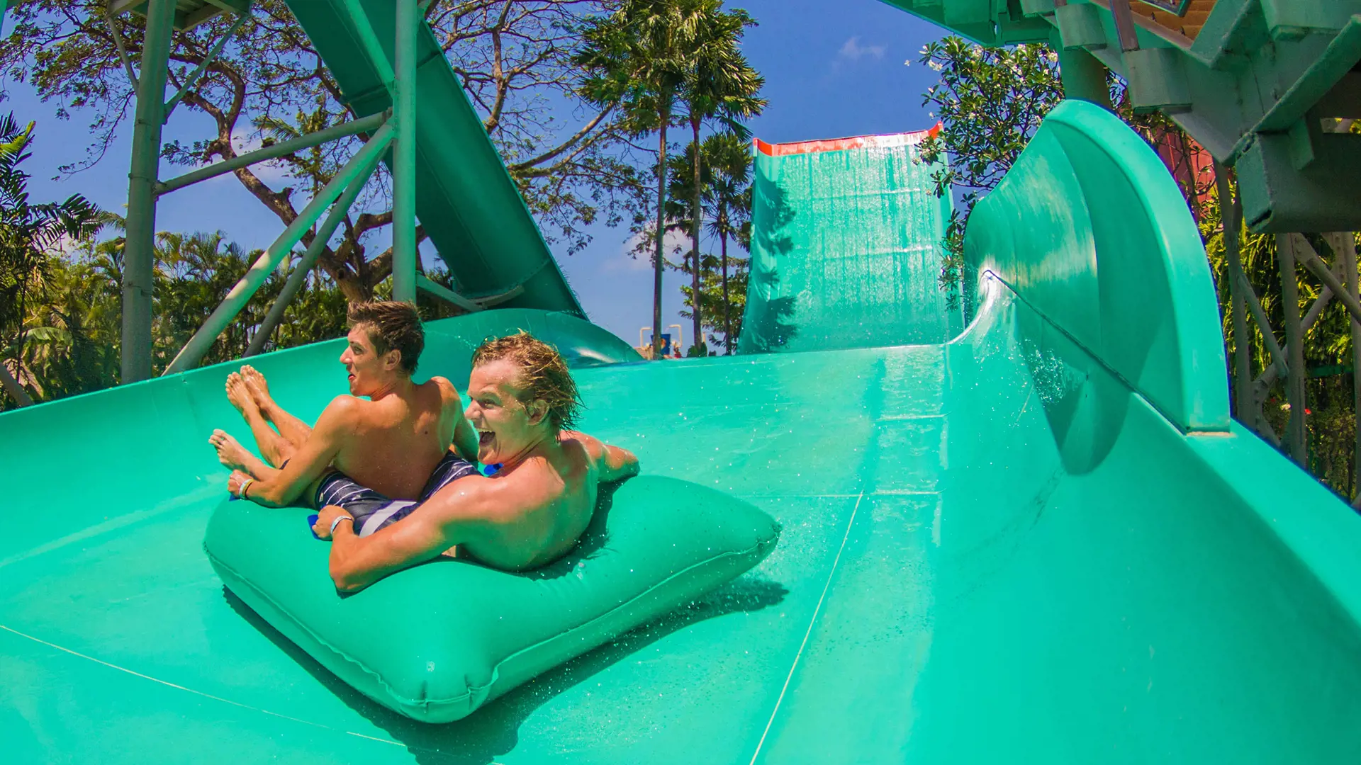 Two friends laughing on an air-mat down a green slide at Waterbom Bali