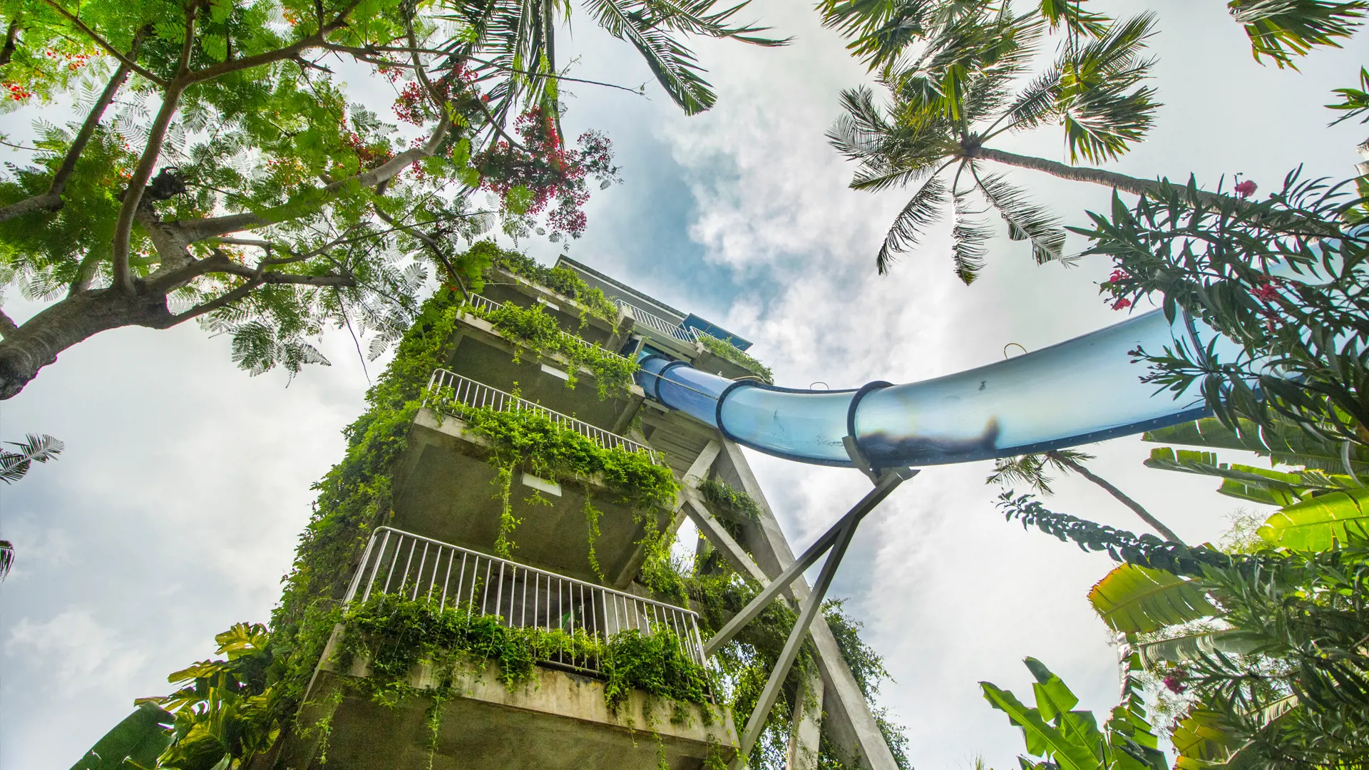 Blue water slide winding down from a vine-covered tower framed by palm trees at Waterbom Bali